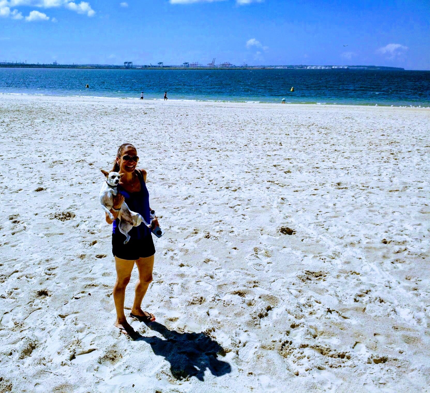 Dion holding a small dog on a bright Bayside beach